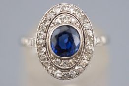 A white metal cluster ring set with a central deep blue sapphire