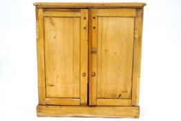 A pine cupboard with two panelled doors with brass handles, enclosing two shelves on plinth base,