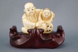 A late 19th century ivory netsuke of an old couple, seen seated and embracing,