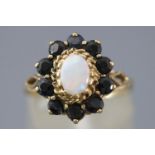 A yellow metal cluster ring set with an oval cabochon opal and surrounded by sapphires.