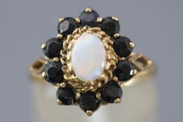 A yellow metal cluster ring set with an oval cabochon opal and surrounded by sapphires.