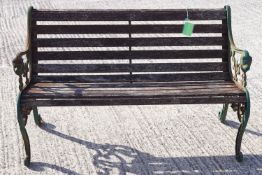 A cast metal and teak slat garden bench with arm supports finishing in a lion's mask,