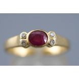 A yellow metal dress ring set with an oval faceted cut ruby and four round cut diamonds.