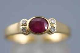 A yellow metal dress ring set with an oval faceted cut ruby and four round cut diamonds.