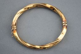 A yellow metal hollow twisted bangle. Hinged clasp with figure of eight safety catch.
