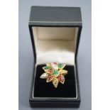 A yellow metal abstract design flower ring set with cabochon cut rubies and emeralds (one chipped)