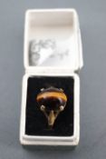 A yellow metal single stone ring. Set with an oval cabochon cut tigers eye.