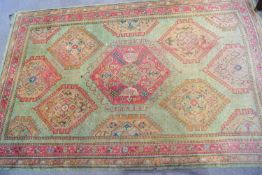 A large Turkish carpet with a series of hooked medallions on a green field within multiple borders,