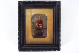 A mid 19th century hand tinted photograph of a soldier in a red tunic with a sabre and a bicorn hat,
