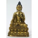A gilt bronze figure of a Buddha sitting meditating in the lotus position on a shaped base