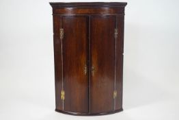 A George III oak and mahogany cross banded bow fronted hanging corner cabinet,