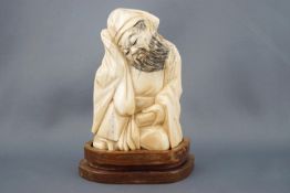 An early 20th century carved ivory figure of a sage shown seated and holding a book,