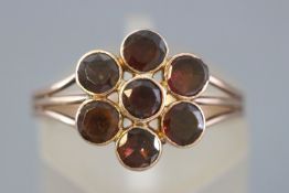 A rose metal flower cluster ring set with round faceted cut garnets.