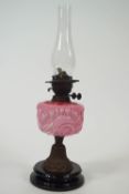 An early 20th century oil lamp with moulded pink glass reservoir, picked out in enamels,