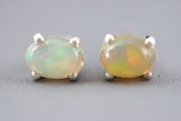 A white metal pair of single stone stud earrings. Each set with an oval cabochon cut Ethiopian opal.