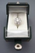 A white metal diamond cluster ring set with a central round brilliant cut diamond