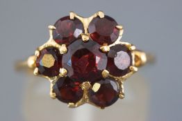 A yellow metal cluster ring set with seven circular faceted cut garnets.