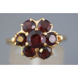 A yellow metal cluster ring set with seven circular faceted cut garnets.
