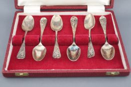 A cased set of six white metal (marks indistinct), Old English picture back tea spoons,