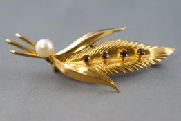 A yellow metal leaf brooch set with four round garnets and finished with a cultured pearl.
