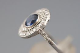 A white metal cluster ring set with a central deep blue sapphire