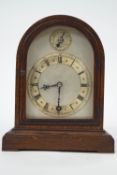 An oak cased mantel clock, the arched silvered dial with fast/slow subsidiary dial,