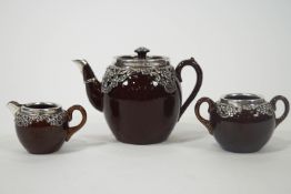 An early 20th century brown glazed pottery tea service with silver mounts,