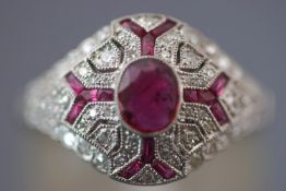 A white metal dress ring. Set with a central oval faceted cut ruby