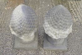 A pair of composite stone pine cone finial ornaments raised on square socles, 55cm high