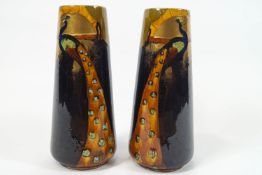 A pair of Phoenix ware pottery vases, each of plain conical form, decorated with a peacock,