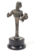 A small metal figure of a man holding a drinks container, raised on a plain wooden base,