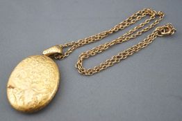 A yellow metal large locket pendant with engraved finish, suspended from a trace link chain.