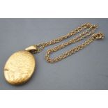 A yellow metal large locket pendant with engraved finish, suspended from a trace link chain.