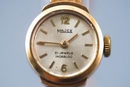 A yellow metal Majex wristwatch. Round silver dial with baton markings.