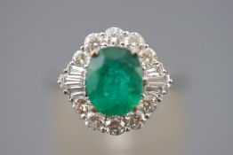 A white metal cluster ring. Set with an oval faceted cut emerald