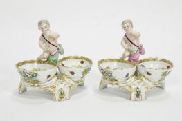 A pair of 19th century Sitzendorf salts, each with a putti above two baskets,