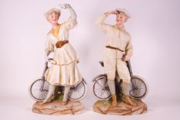 A pair of Heubach coloured decorated bisque cycling figures of a gentleman and a lady,