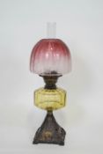 A glass and iron oil lamp with a cranberry shade,