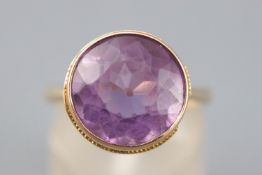 A yellow metal single stone ring. Set with a round faceted cut amethyst