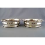 A pair of silver wine coasters with gadrooned edges over bellied bodies on turned hardwood bases,