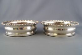 A pair of silver wine coasters with gadrooned edges over bellied bodies on turned hardwood bases,