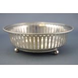 A silver bowl, of plain form with bead edge over a pierced body, raised on three ball feet,