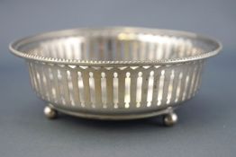 A silver bowl, of plain form with bead edge over a pierced body, raised on three ball feet,