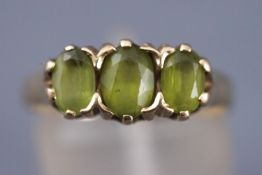 A yellow metal ring set with three oval faceted cut peridots. Hallmarked 9ct gold, Sheffield, 1990.