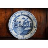 An 18th century English Delft charger painted with figures on a bridge,