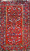 A rug with stylised flowers and leaves on a red ground within three borders,