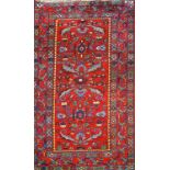 A rug with stylised flowers and leaves on a red ground within three borders,