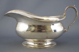 A silver sauce boat, of bellied oval form with milled edging and C scroll handle, Birmingham 1932,
