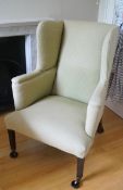 A green upholstered wing back armchair on square tapering legs with brass casters