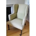 A green upholstered wing back armchair on square tapering legs with brass casters